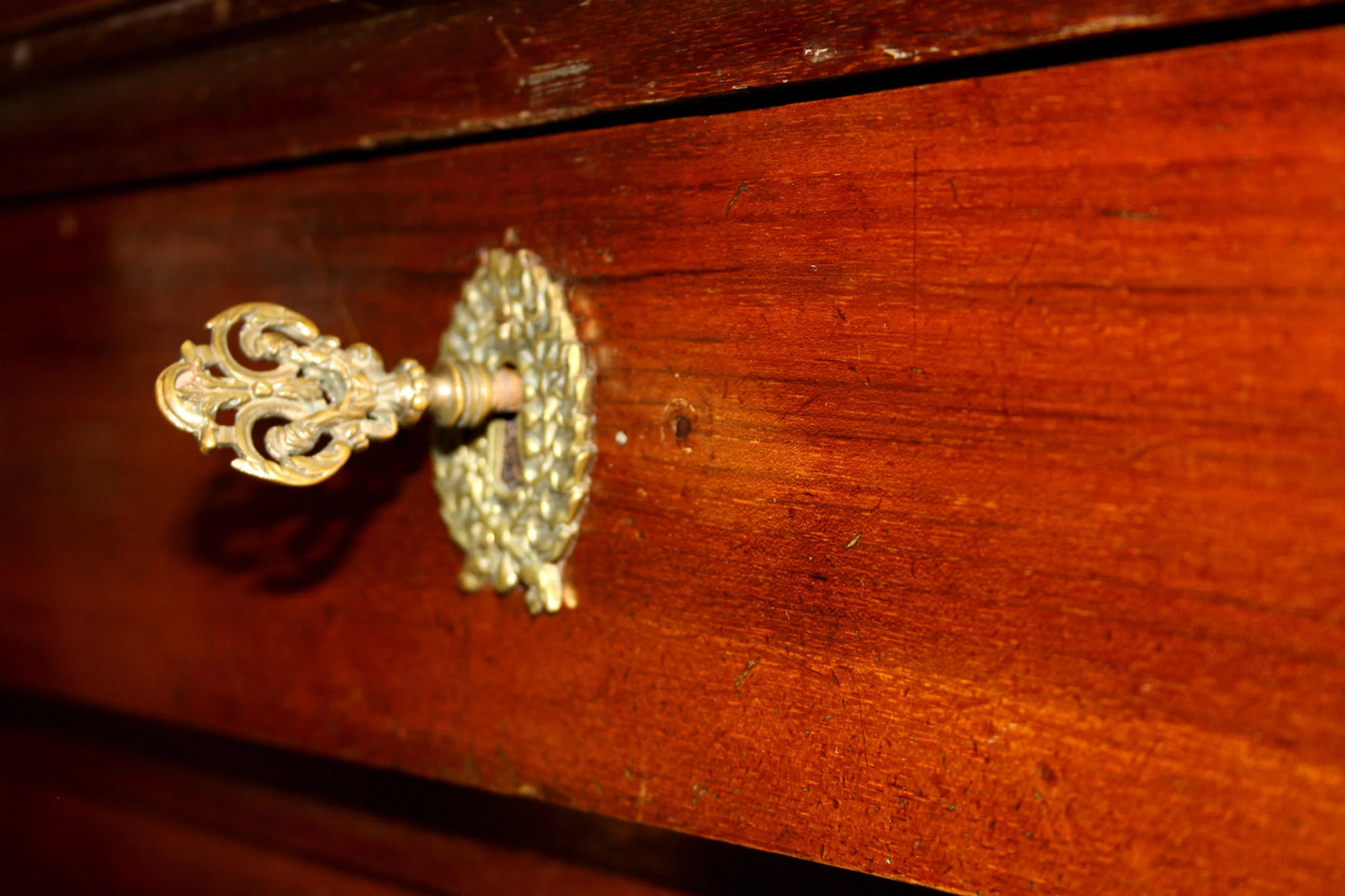 An ornate brass key inside a wooden drawer of a cassettiera impero with bronzo xix secolo details showcasing artigianato italiano d’epoca