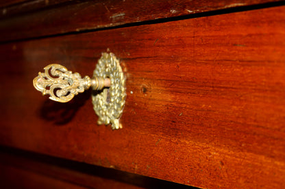 An ornate brass key inside a wooden drawer of a cassettiera impero with bronzo xix secolo details showcasing artigianato italiano d’epoca
